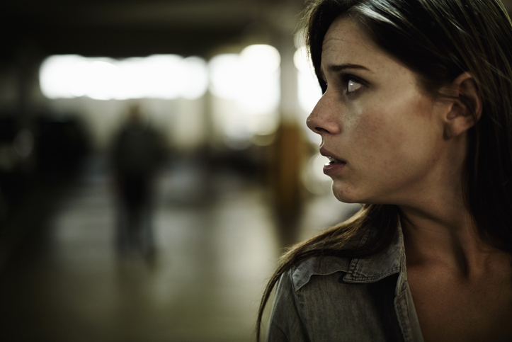 A terrified young woman in an underground parking garage being followed by a sinister man